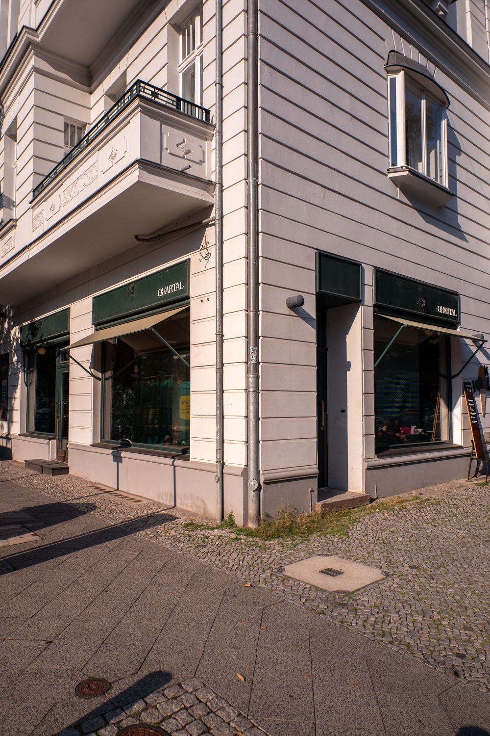 Die Eckfassade mit den dunkelgrünen Markisen über den Schaufenstern, QUARTAL in kleinen Lettern auf der Blende.