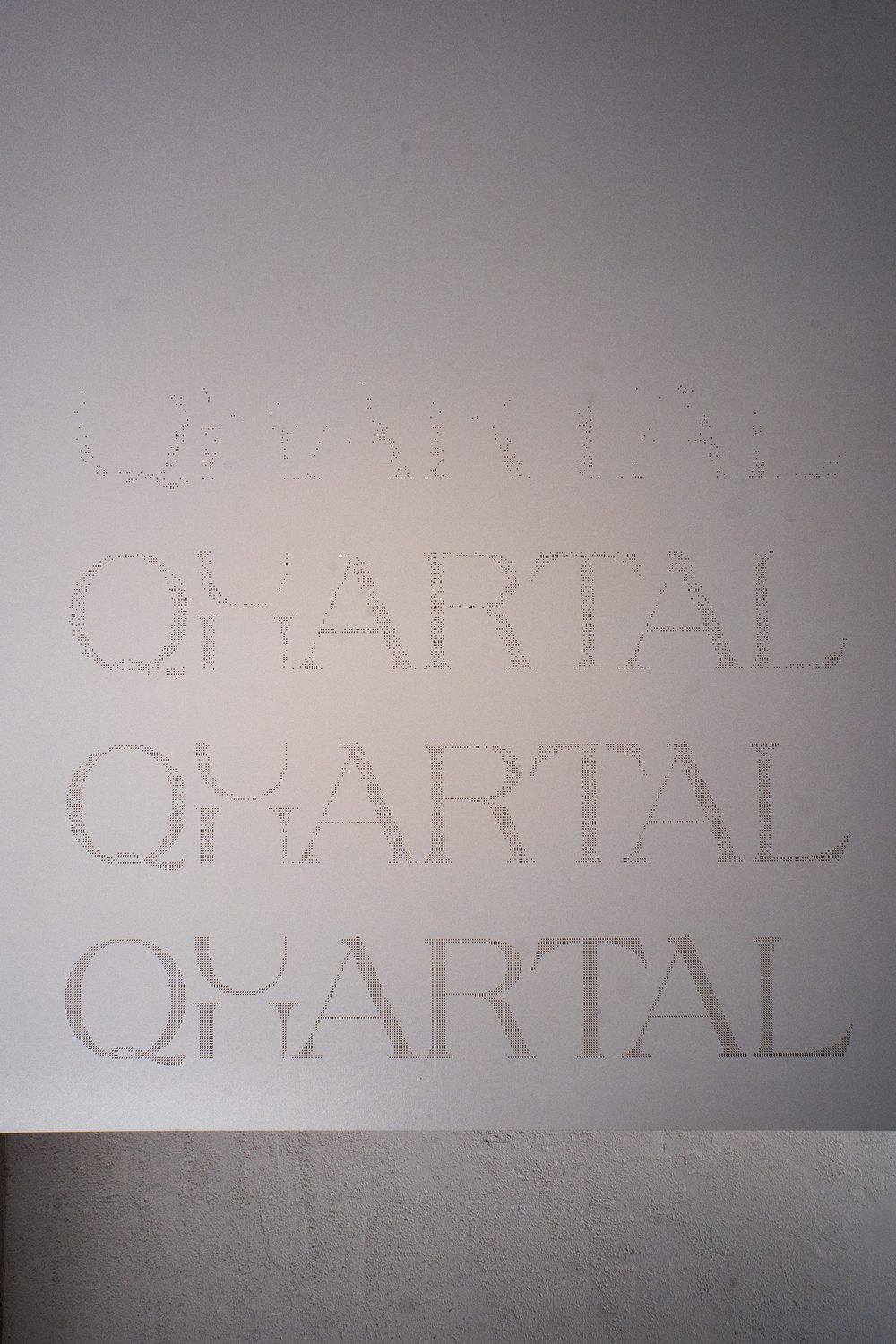 Der Schriftzug QUARTAL, mehrfach übereinander in den hellen Wandputz geprägt, im Streiflicht.