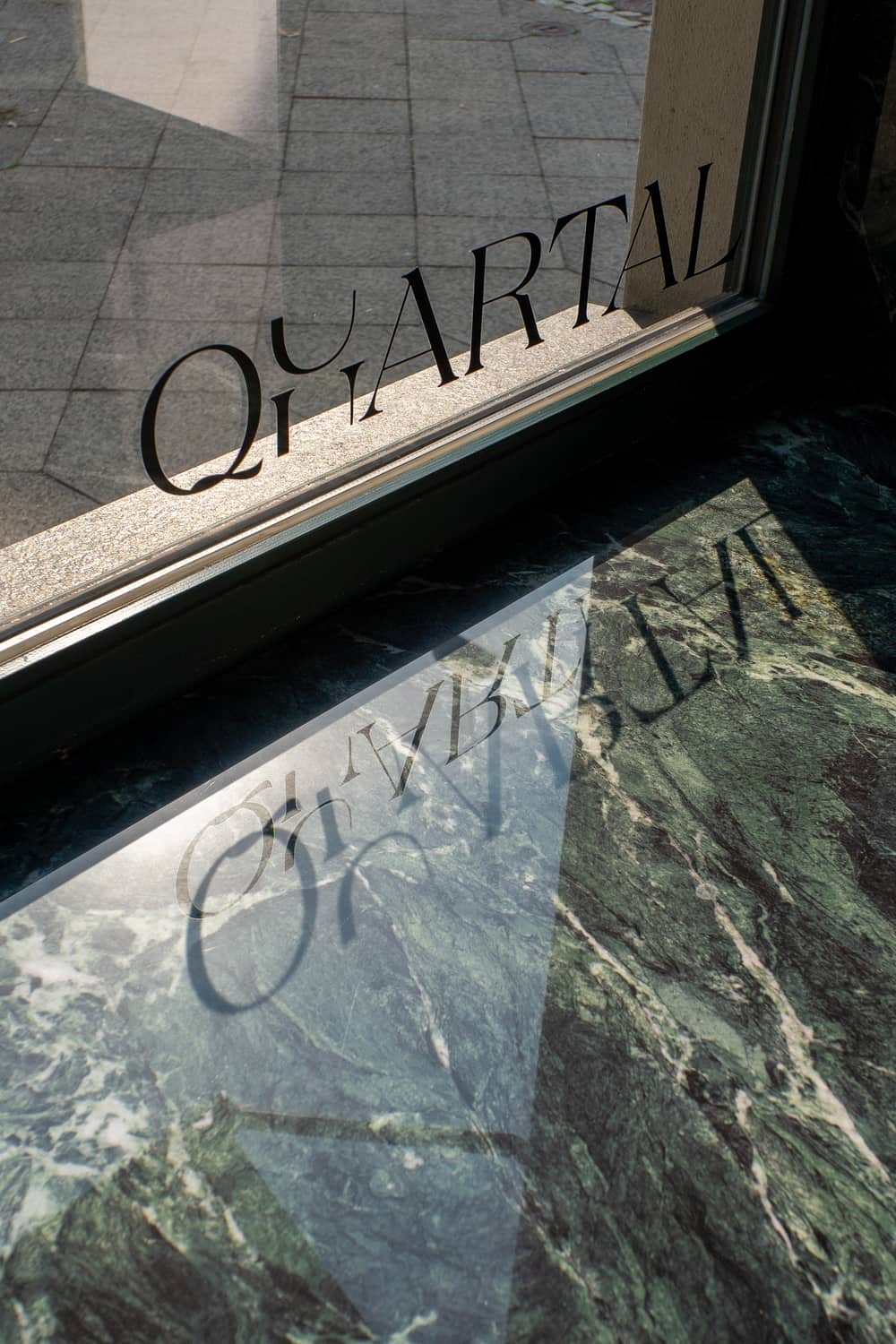 Der Schriftzug Quartal auf der Glasfront, gespiegelt in der geäderten Fensterbank.